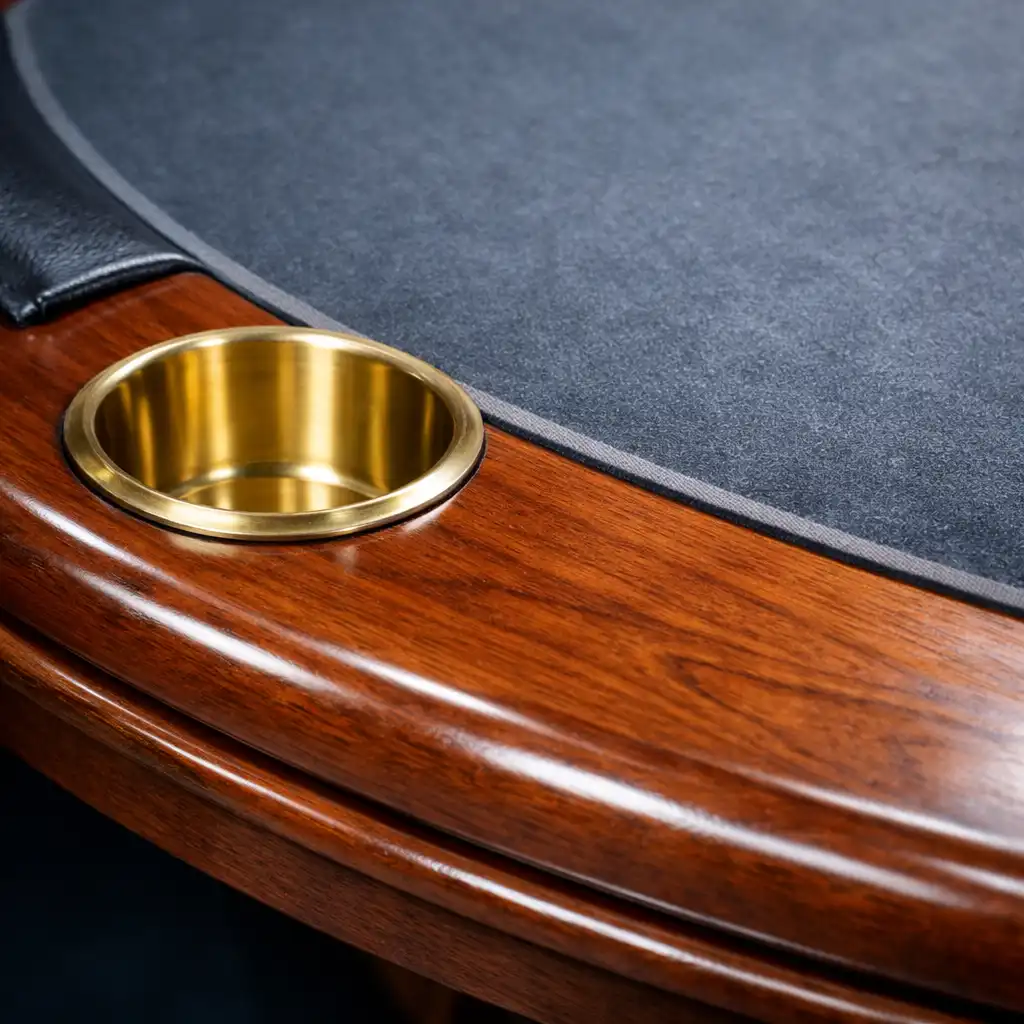 Detailed close-up of a poker table edge showing the polished wooden rim, a brass cup holder, and the deep slate felt surface.